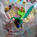 A mixed media collage features a duck figurine, pipe cleaners, tissue paper, gold foil, and colourful chalk or crayon marks on brown paper labelled "DUCK'S DINNER.