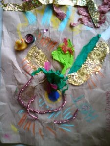 A mixed media collage features a duck figurine, pipe cleaners, tissue paper, gold foil, and colourful chalk or crayon marks on brown paper labelled "DUCK'S DINNER.