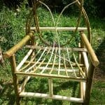 A handmade wooden chair with a curved backrest and open slatted seat, placed on grass in a garden setting.