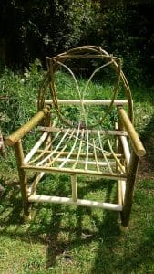 A handmade wooden chair with a curved backrest and open slatted seat, placed on grass in a garden setting.